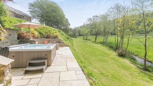 A hot tub with a stone patio, a grassy lawn, and a view of a rural landscape.