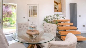 A modern living room with a glass table, cushioned chairs, a wooden staircase, and a door leading outside. - 2 Bed in Kelly (oc-k29333) (Kelly)