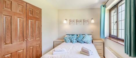 A bedroom with a bed, a wooden wardrobe, a nightstand, a wall-mounted light, a window with curtains, and a radiator.