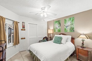 A bedroom with a bed, a ceiling fan, a nightstand, and artwork on the wall.