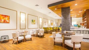 A modern hotel lobby with a wooden floor, white and yellow chairs, and framed artwork on the walls.