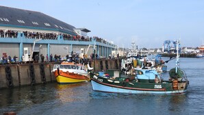 Un puerto con barcos amarrados y un edificio con una multitud de personas en la cubierta superior.