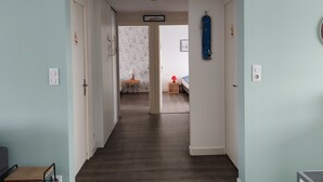 Un pasillo con piso de madera que conduce a un dormitorio con cama y mesita de noche.