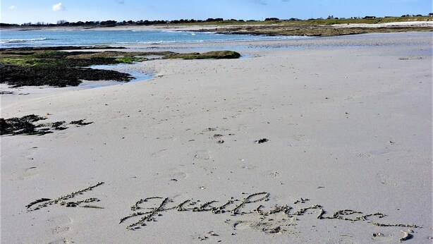 Una playa con huellas y la palabra 'le gentilhomme' escrita en la arena.