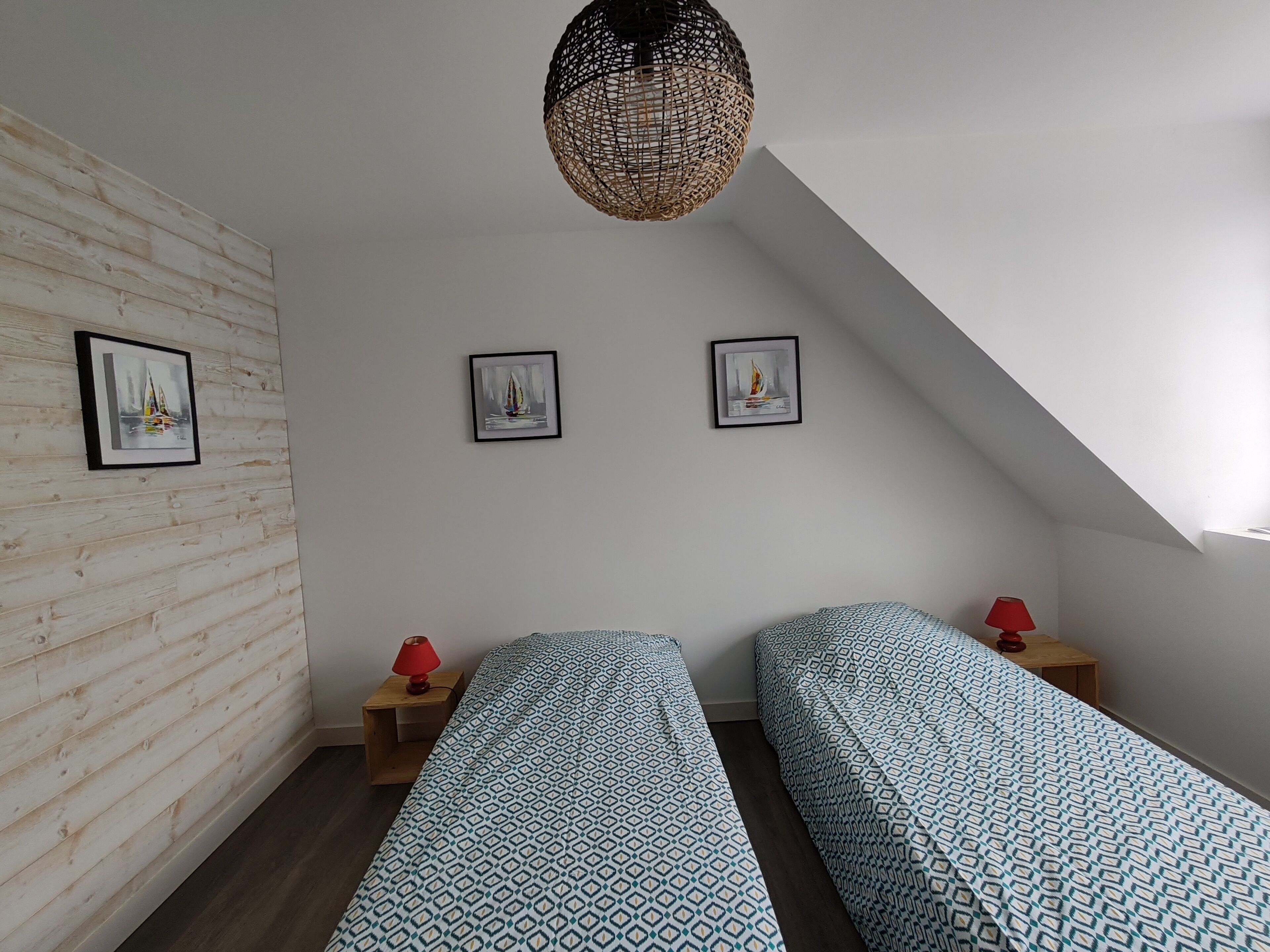 A bedroom with two beds, wooden walls, and framed pictures on the wall.