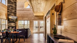 Un interior de madera con comedor, chimenea y vistas a través de puertas de vidrio.