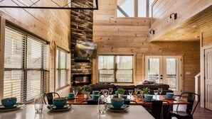 Interior de una cabaña de madera con comedor, chimenea y un rincón de descanso acogedor.