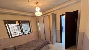 A bedroom with a bed, a window with bars, a door, and a chandelier. - Comfortable Stay (Amman)