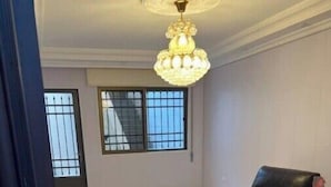 A spacious room with a black leather chair, a chandelier, and large windows with metal bars. - Comfortable Stay (Amman)