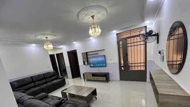 A modern living room with a black leather sofa, a wooden coffee table, a flat-screen TV, and a decorative mirror. - Comfortable Stay (Amman)