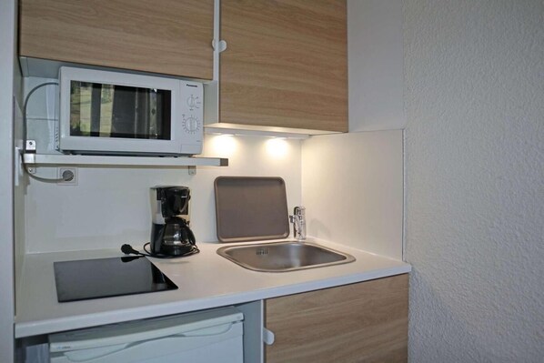 A compact kitchenette with a microwave, coffee maker, and sink.