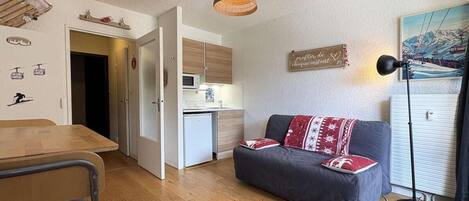 A compact living space with a kitchenette, a dining area, and a sofa with a decorative pillow.
