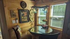 Un interior de madera con una mesa redonda de cristal, dos sillas, un reloj de pared, obras de arte enmarcadas y un farol decorativo.