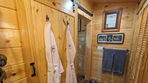 Interior de una cabaña de madera con un armario de madera, dos albornoces blancos con personajes de caricatura, un certificado enmarcado en la pared y un perchero.