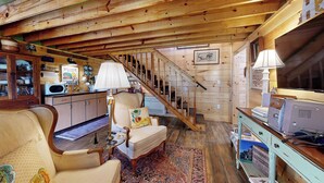 Un acogedor interior de cabaña con techo de madera, una escalera, una zona de comedor y una sala de estar con sofá y mesa de centro.
