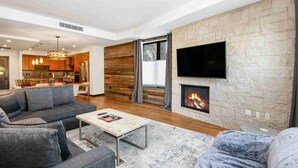 A modern living room with a fireplace, a sofa, a coffee table, and a TV mounted on the wall. - Modern 2 Bedroom Luxury Condo in Lionshead Village (Vail)