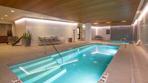 A modern indoor swimming pool with clear water, a wooden ceiling, and a seating area with a sofa and plants. - Modern 2 Bedroom Luxury Condo in Lionshead Village (Vail)