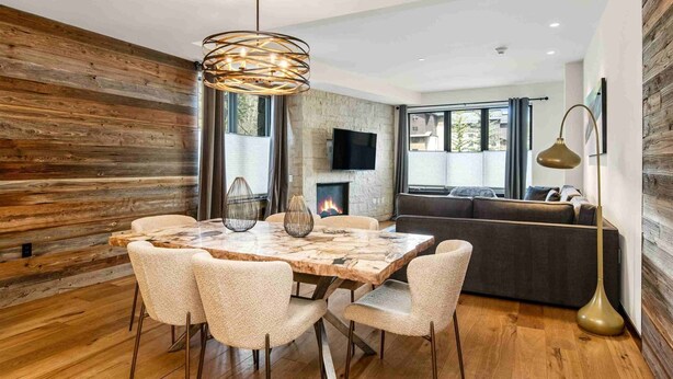 A modern dining area with a wooden table, upholstered chairs, and a hanging light fixture. - Modern 2 Bedroom Luxury Condo in Lionshead Village (Vail)