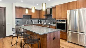 A modern kitchen with wooden cabinets, stainless steel appliances, and a central island with bar stools. - Modern 2 Bedroom Luxury Condo in Lionshead Village (Vail)