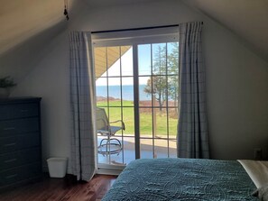Un dormitorio con cama, cómoda, silla y vistas al exterior a través de una puerta corrediza de vidrio.