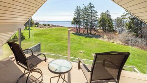 A balcony with two chairs and a table, overlooking a grassy area with trees and a body of water. - On one of the 𝗜𝘀𝗹𝗮𝗻𝗱'𝘀 𝗯𝗲𝘀𝘁 𝗯𝗲𝗮𝗰𝗵𝗲𝘀; enjoy sun, sand & sea! (Bedeque)