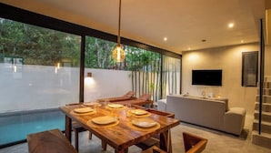 Un espace repas moderne avec une table en bois dressée pour quatre personnes, un canapé et un téléviseur fixé au mur.