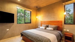 Une chambre moderne avec un grand lit, un téléviseur fixé au mur et une fenêtre donnant sur la verdure.