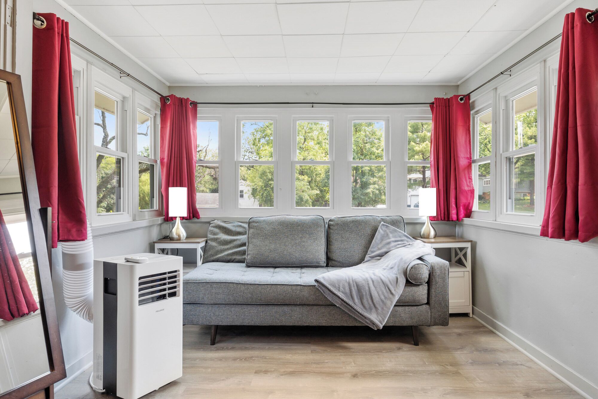 A room with a grey sofa, red curtains, and a window with a view of trees.