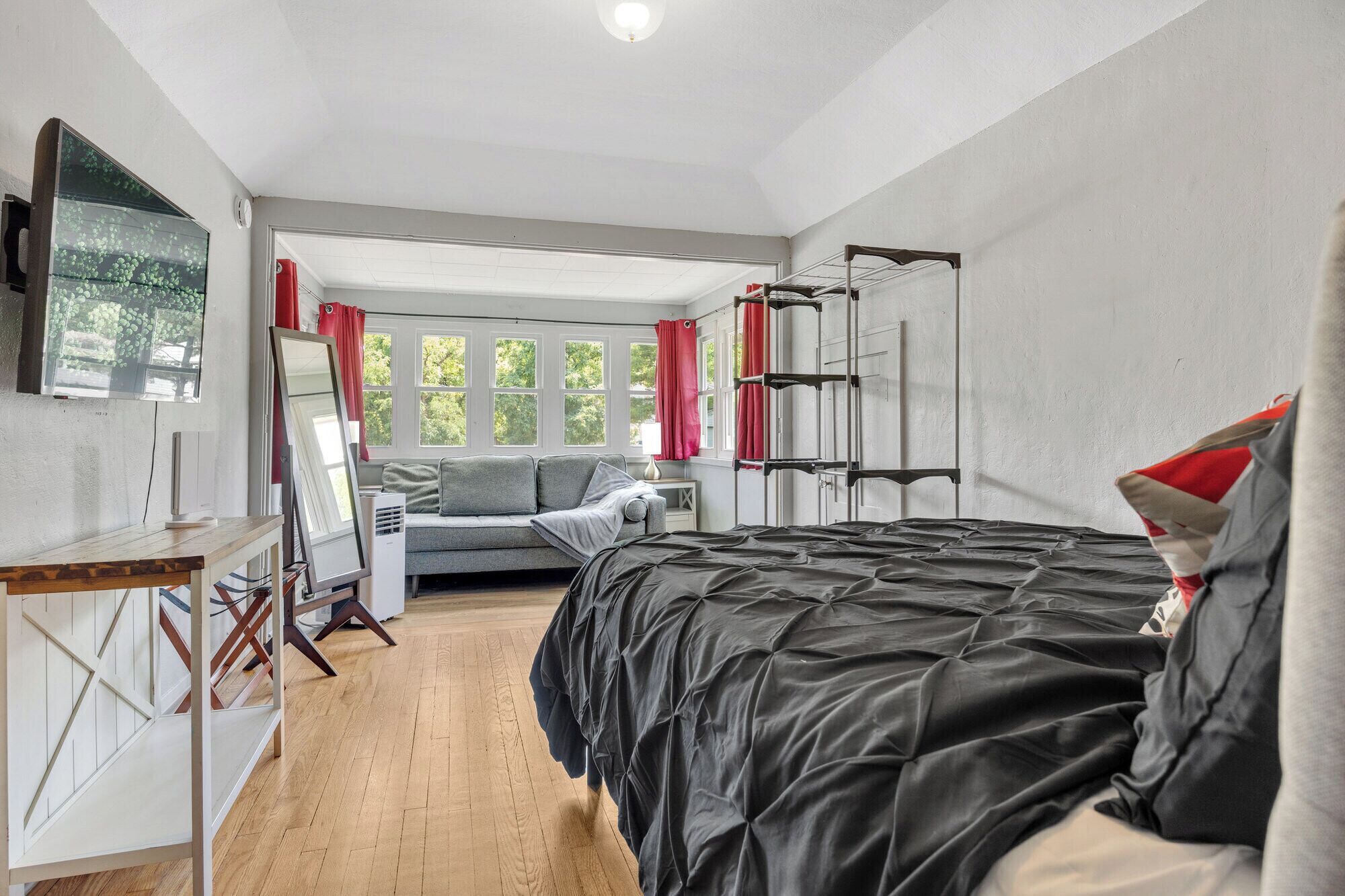 A bedroom with a bed, a desk, a chair, a sofa, and a window with curtains.