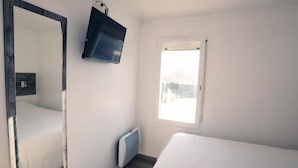 A bedroom with a bed, a large mirror, a TV mounted on the wall, and a window with a view of the outdoors. - Fasthôtel Albertville (Albertville)