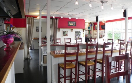 A restaurant with wooden chairs and tables, a red accent wall, and a view of the outdoors through large windows.
