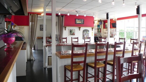 A restaurant with wooden chairs and tables, a red accent wall, and a view of the outdoors through large windows. - Fasthôtel Albertville (Albertville)
