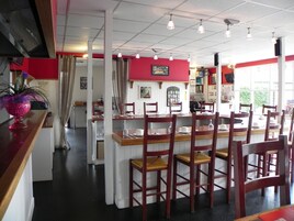 Un restaurant avec des chaises et des tables en bois, un mur d’accent rouge et une vue sur l’extérieur grâce à de grandes fenêtres.
