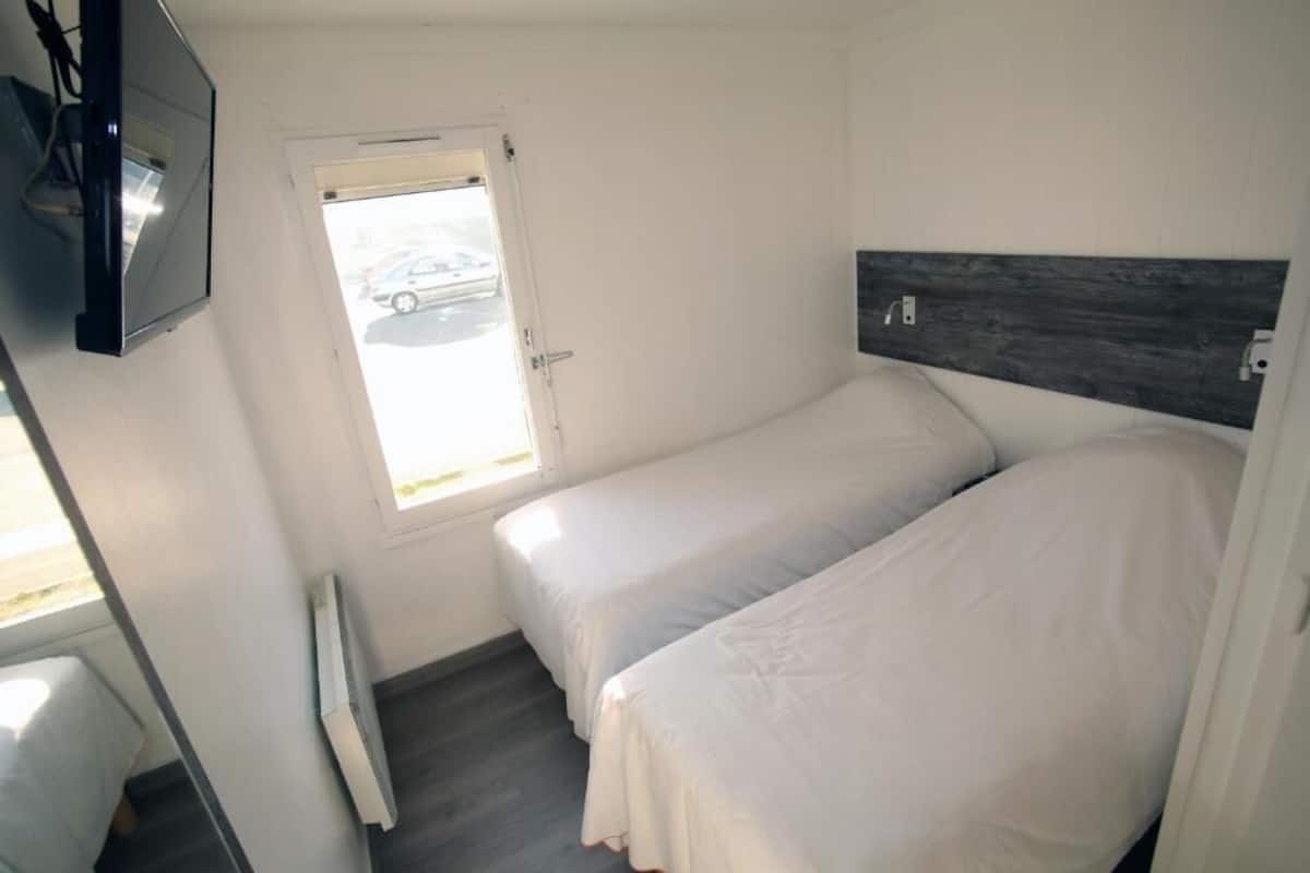 A small, clean room with two single beds, a window with a view of a parking area, and a mounted TV.