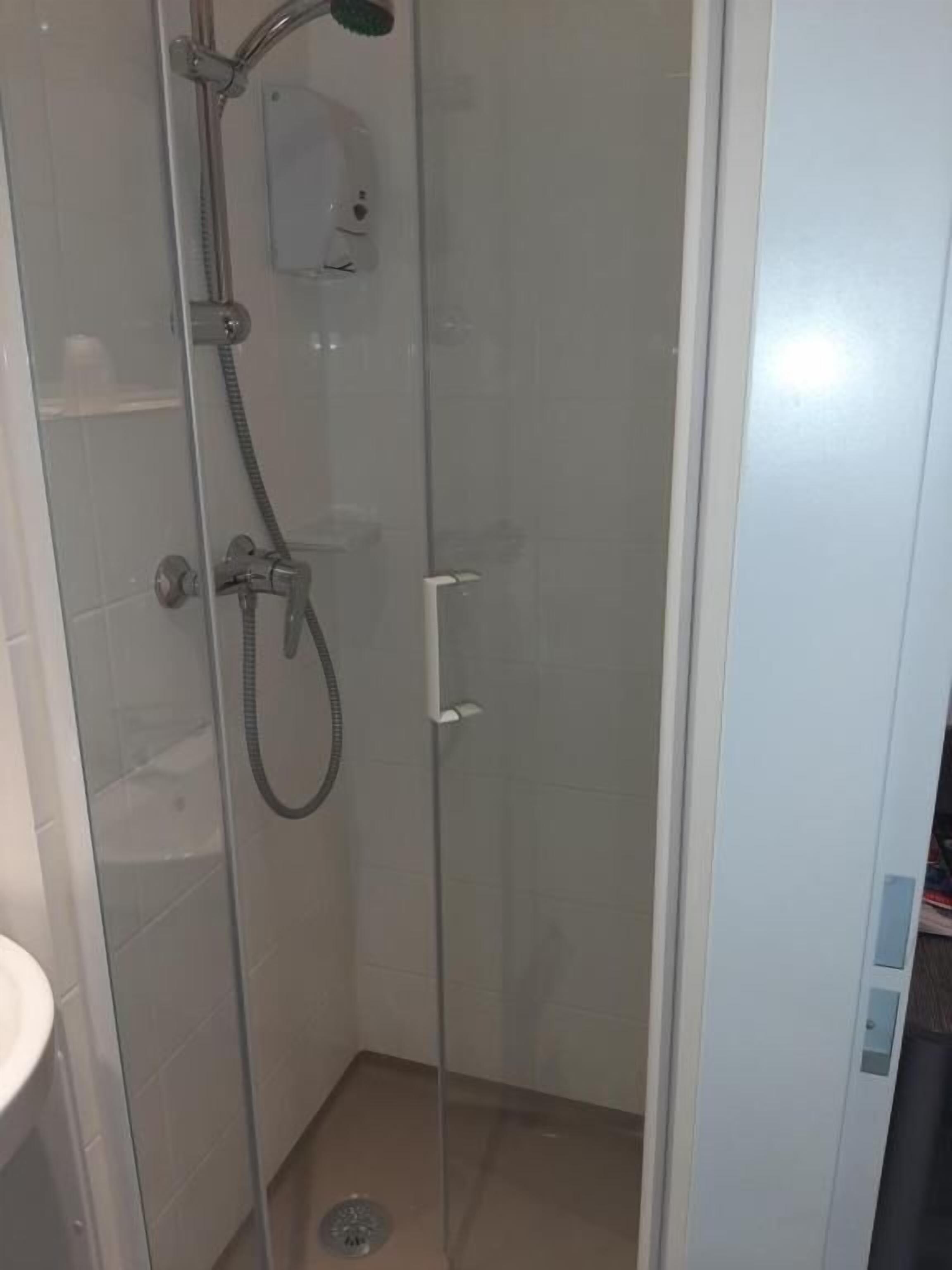 Eine Duschkabine mit Glaswänden, einer Handbrause, einer fest installierten Bedienarmatur und einem Ablauf im Boden.
