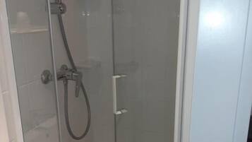 Eine Duschkabine mit Glaswänden, einer Handbrause, einer fest installierten Bedienarmatur und einem Ablauf im Boden.