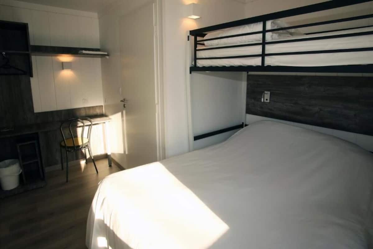 A bunk bed with a wooden headboard, a small desk with a chair, and a white wall-mounted cabinet.