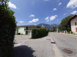 Une vue de rue avec un bâtiment sur lequel on peut voir une enseigne indiquant qu’il s’agit d’un hôtel. On aperçoit des montagnes à l’arrière-plan et le ciel est dégagé.