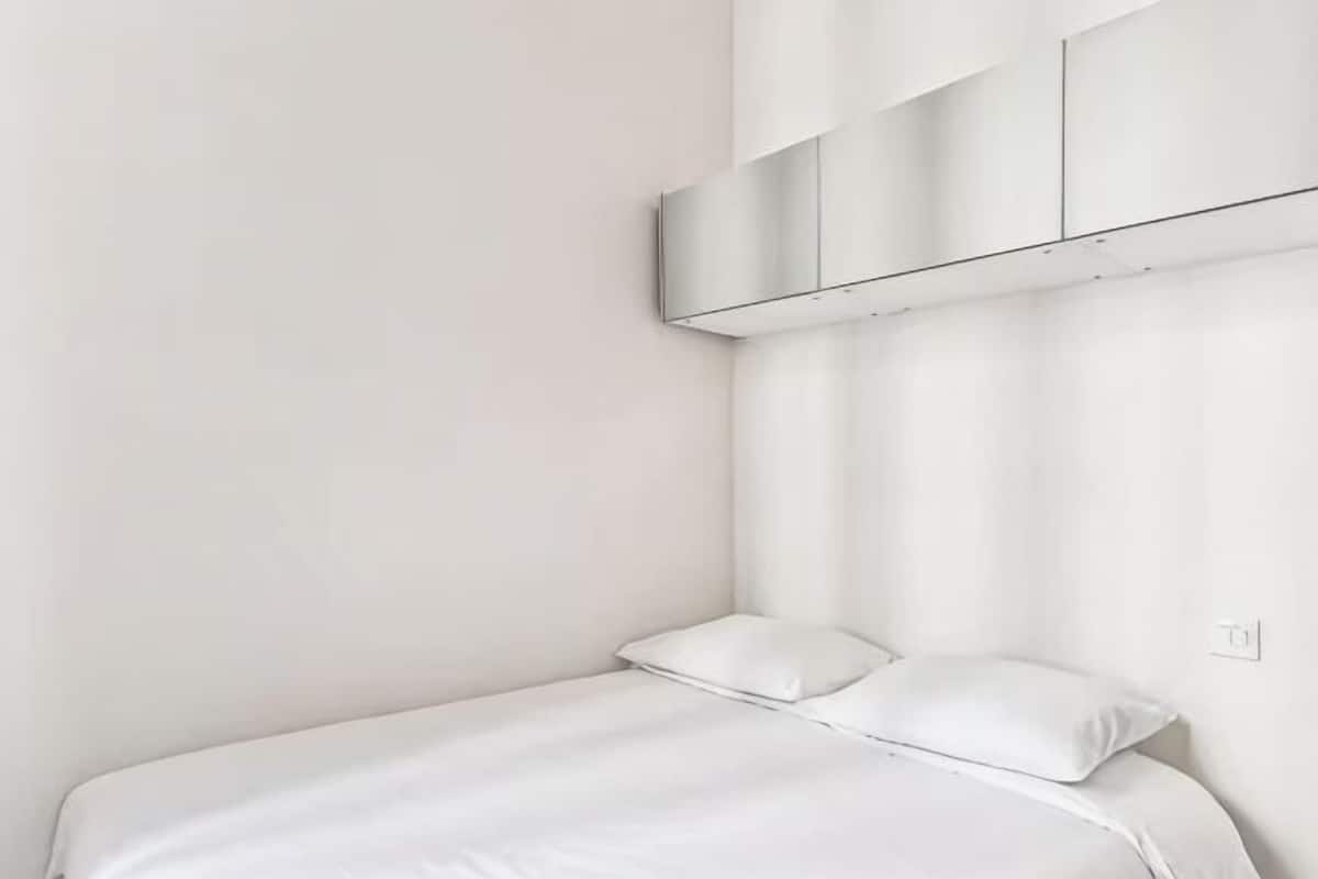 Una cama blanca con dos almohadas, una pared blanca y un techo blanco.