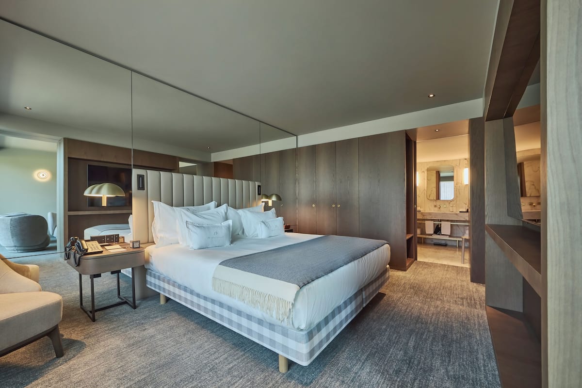 A modern hotel room with a large bed, bedside tables, a desk, and a mirror.