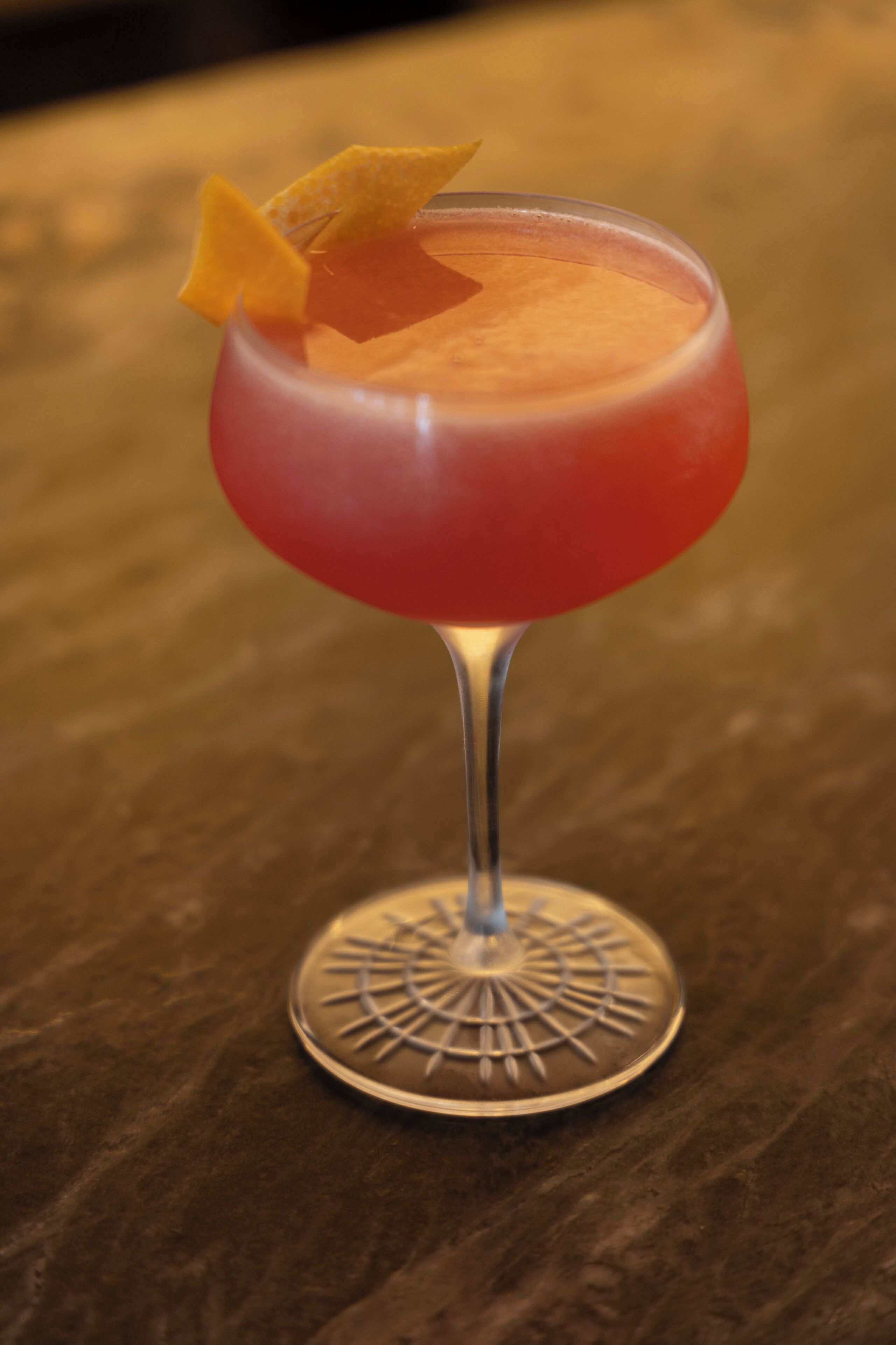 A cocktail in a stemmed glass with a decorative garnish on a wooden surface.