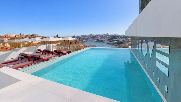A rooftop infinity pool with red lounge chairs and umbrellas, overlooking a cityscape and harbor. - Altis Porto Hotel, member of Preferred Hotels & Resorts – L.V.X. (Porto)