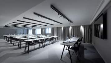 A conference room with multiple tables and chairs, ceiling lights, and a large window with curtains.