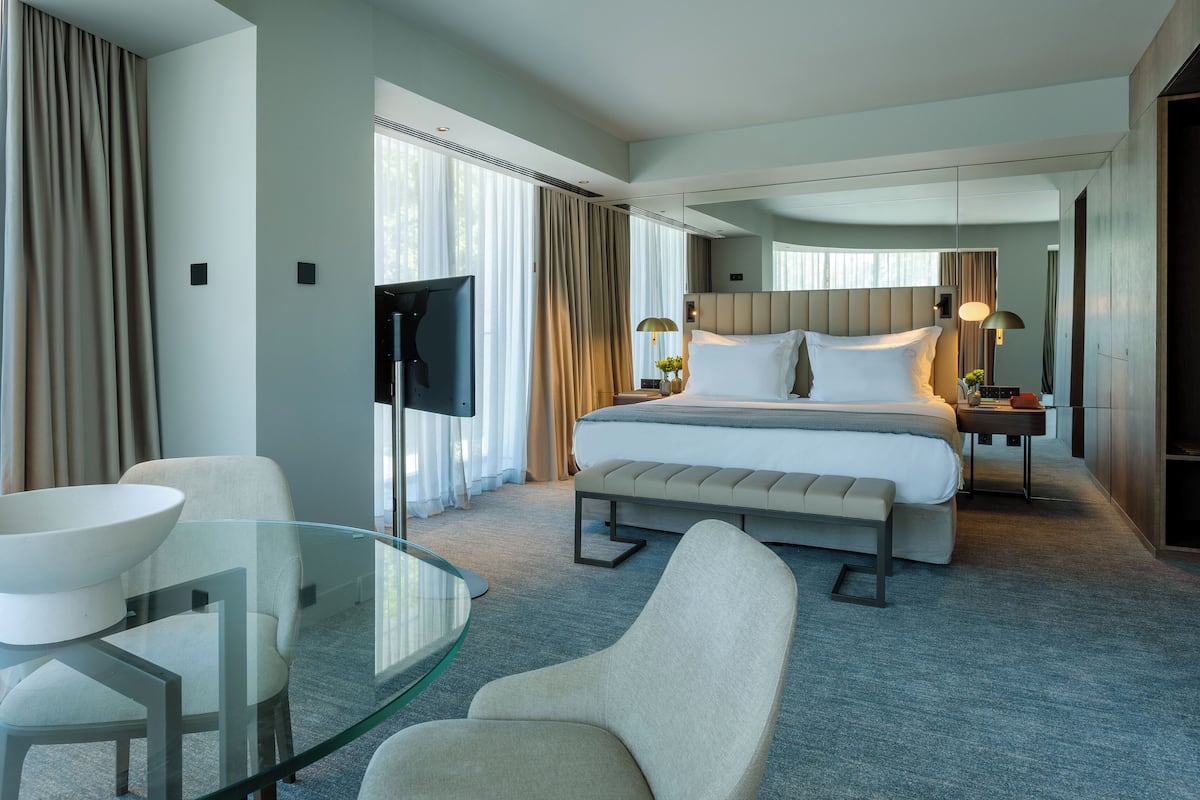 A modern hotel room with a large bed, a glass table, and a seating area.