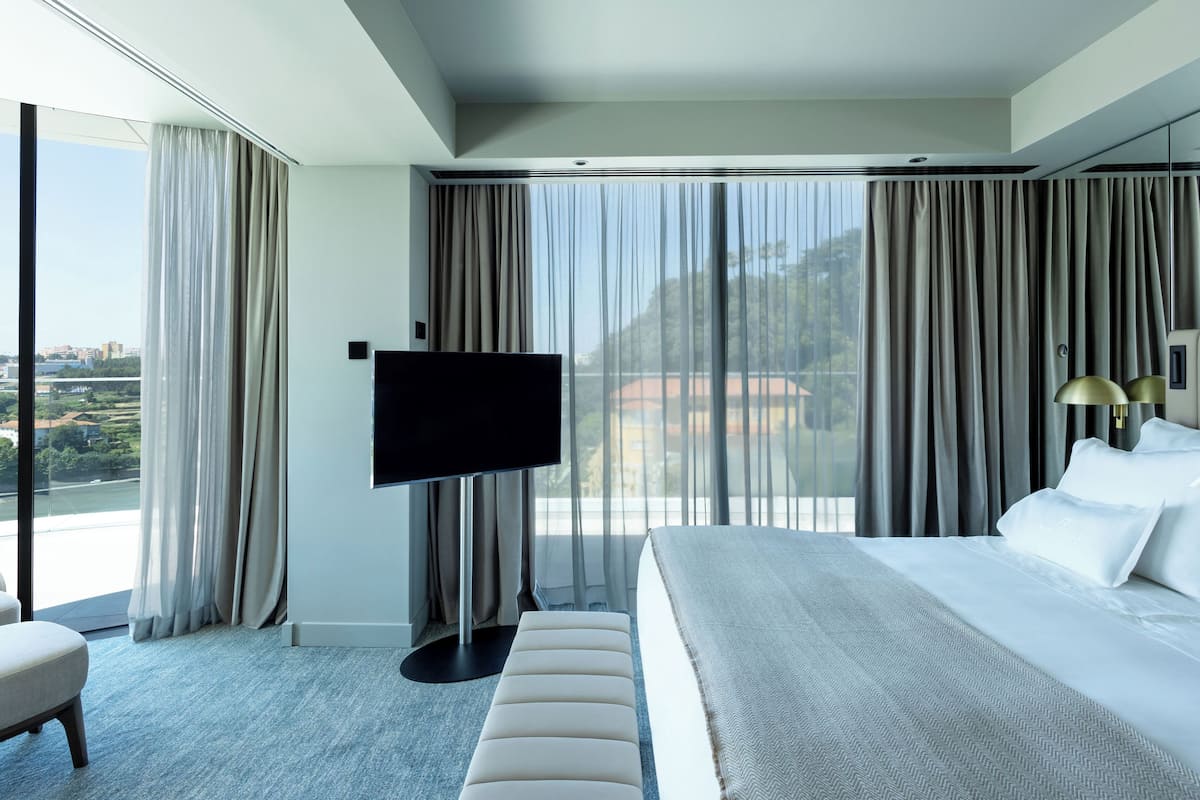 A modern hotel room with a large bed, a flat-screen TV, a sofa, and a view of the city.