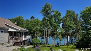 Ein eingeschossiges Haus mit Veranda und Deck, umgeben von Wald und See.