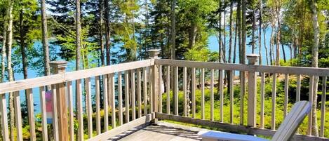 Un terrazzo in legno con poltrone Adirondack e vista su una foresta e un lago.