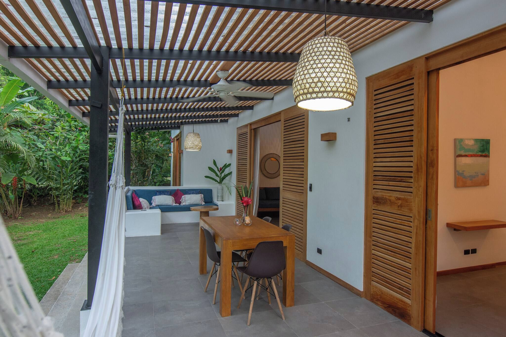 A covered outdoor seating area with a table and chairs, a ceiling fan, and a hanging light fixture.