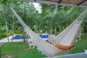 A hammock in a lush garden with a pool in the background.