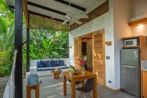 A modern kitchen with a built-in microwave and refrigerator, a wooden dining table with chairs, and a seating area with a blue sofa and a small table. - Tres Lodge Resort Private Pool (Puerto Viejo de Talamanca)